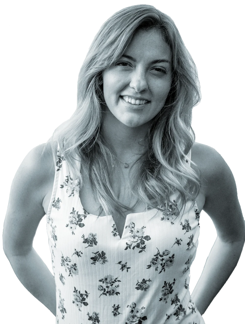 A woman with long wavy hair smiling, wearing a floral sleeveless top, and a necklace, posing with her hands on her hips.
